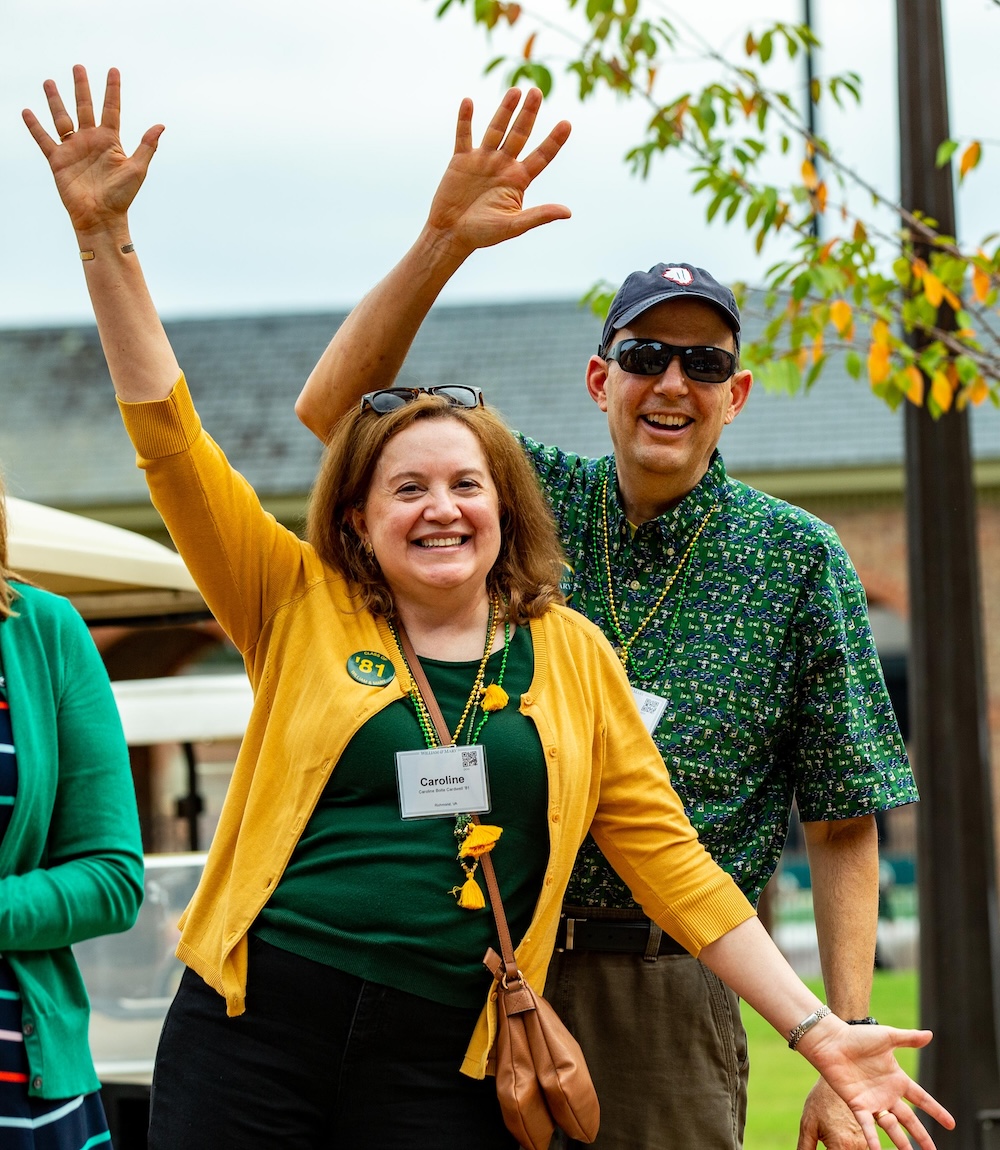 Two alumni in green and gold cheer facing the camera